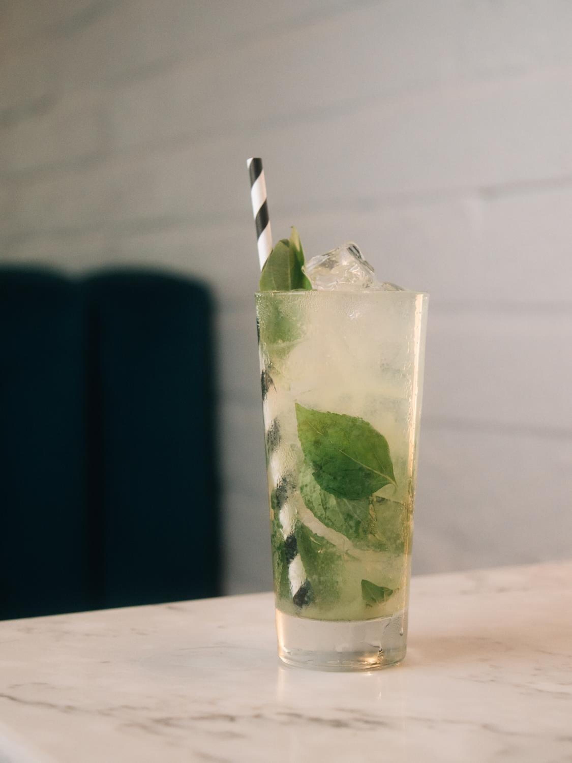 A glass with a striped straw, containing ice and mint leaves, on a marble surface.