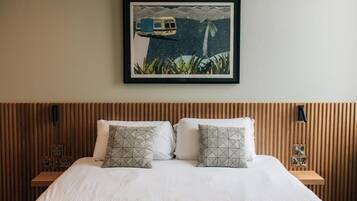 A neatly made bed with two pillows, a framed picture above it, and a wooden headboard.