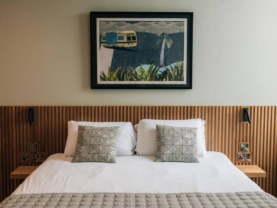 A neatly made bed with two pillows, a framed picture above it, and a wooden headboard.