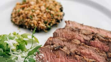 Um prato com uma fatia de bife, acompanhado de legumes e um guarnição à base de grãos.