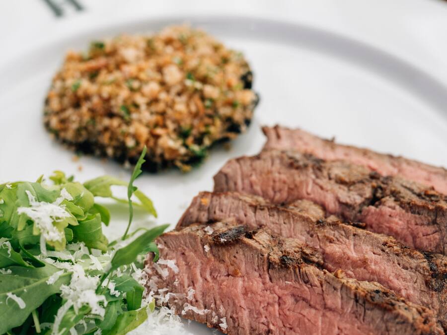 A plate with a slice of steak, a side of greens, and a grain dish.