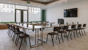 Un salón de conferencias con varias mesas y sillas, ventanas amplias y una televisión instalada.