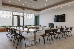 Un salón de conferencias con varias mesas y sillas, ventanas amplias y una televisión instalada.
