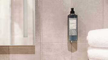 A bathroom with a hand soap dispenser mounted on the wall, a white towel stacked on a wooden surface, and a shower curtain.