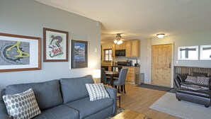 A living room with a gray sofa, patterned pillows, a wooden coffee table, and a dining area with chairs and a table. - Ridgecrest 202 2 Bedroom Condo by RedAwning (Steamboat Springs)