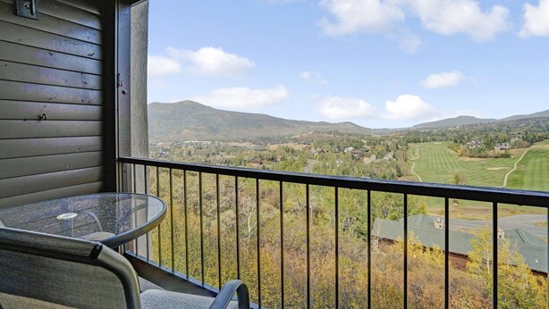 A balcony with a glass table and chair, overlooking a scenic landscape with mountains and a golf course. - Ridgecrest 202 2 Bedroom Condo by RedAwning (Steamboat Springs)