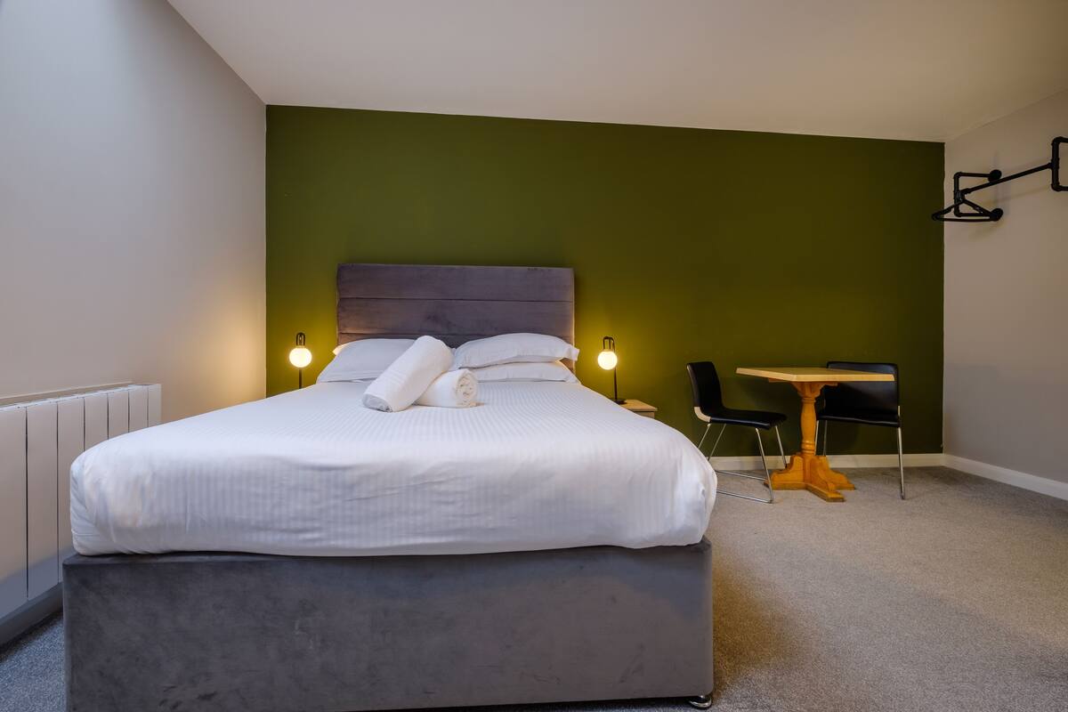 Une chambre d’hôtel moderne avec un grand lit, des lampes de chevet, une petite table et des chaises.