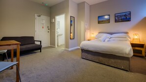 A bedroom with a bed, a sofa, a table, and a nightstand with a lamp. - Station Lodge (Windermere)