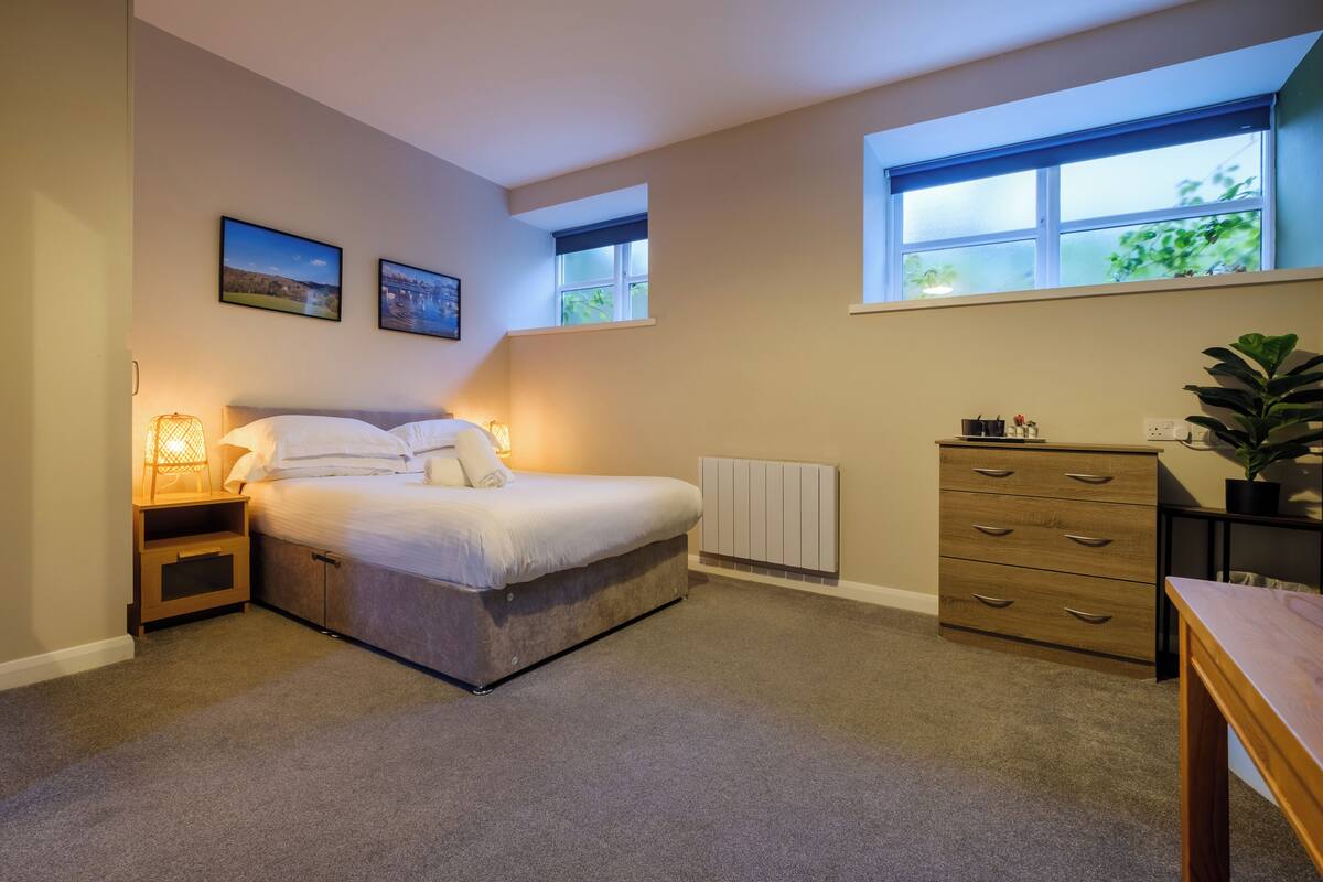 Une chambre à coucher comprenant un lit, des tables de chevet, une commode, une fenêtre et un radiateur.