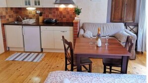 Eine kompakte Küche mit weißen Schränken, einem Herd und einem Spülbecken. Es gibt einen Essbereich mit einem Holztisch und Stühlen sowie ein Sofa.
