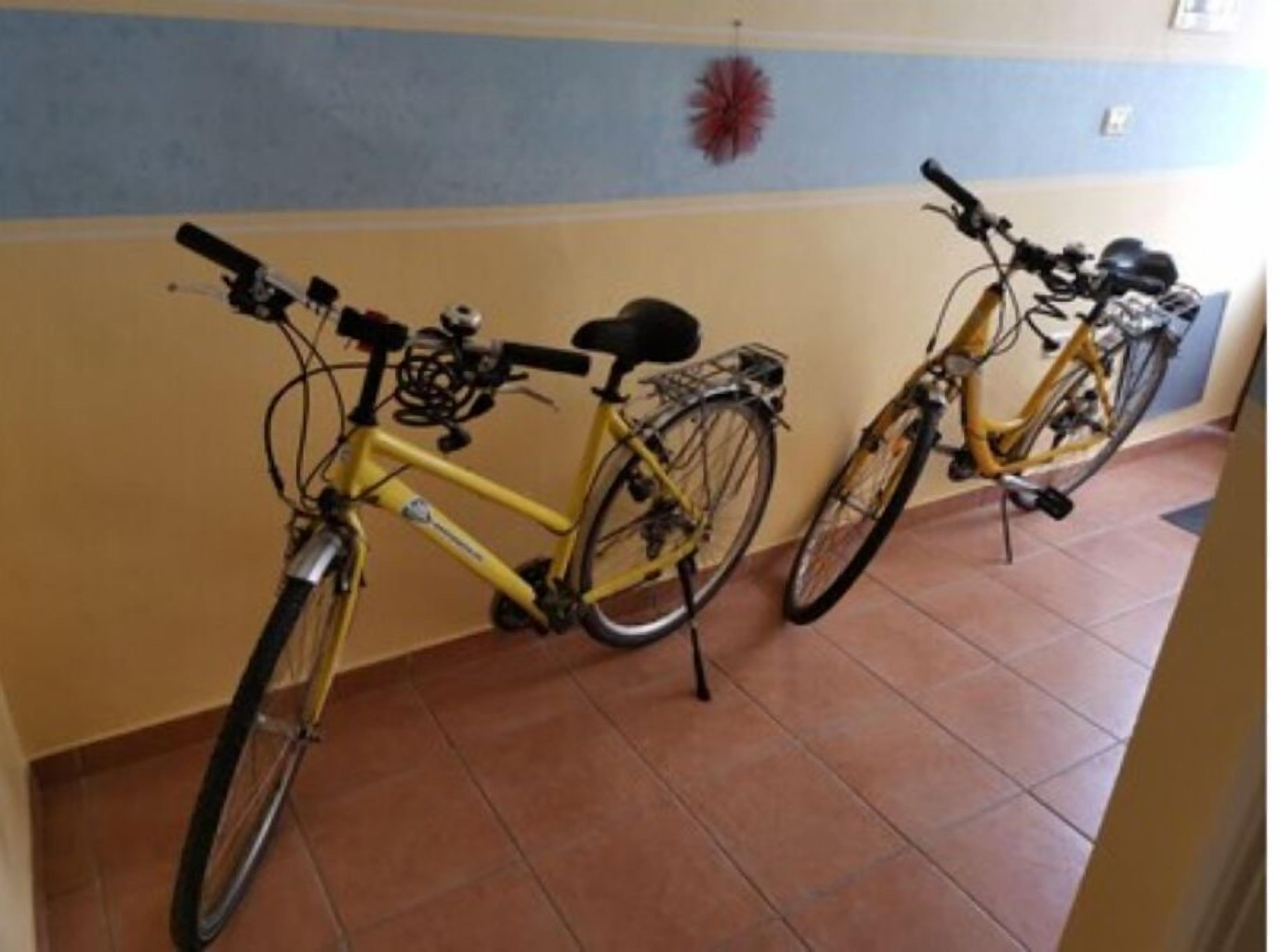 Duas bicicletas estacionadas dentro de um espaço, encostadas a parede com chão de azulejos.