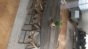 Ein moderner Essbereich mit Holztisch und -stühlen, einer Topfpflanze und einer Couch mit Kissen.