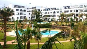 Un hôtel composé de plusieurs bâtiments blancs, avec une piscine centrale et des palmiers.