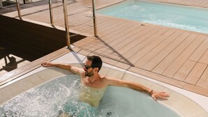 Um homem em uma banheira de hidromassagem com vista para o mar e um espaço de deck.