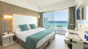 Quarto de hotel com cama, mesa de cabeceira, escrivaninha, cadeira e vista para o mar.