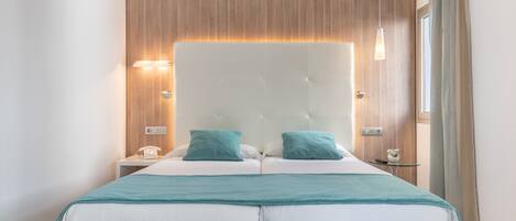 A modern bedroom with a large bed, two bedside tables, a bedside lamp, and a window with curtains.