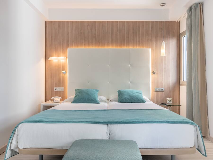 A modern bedroom with a large bed, two bedside tables, a bedside lamp, and a window with curtains.