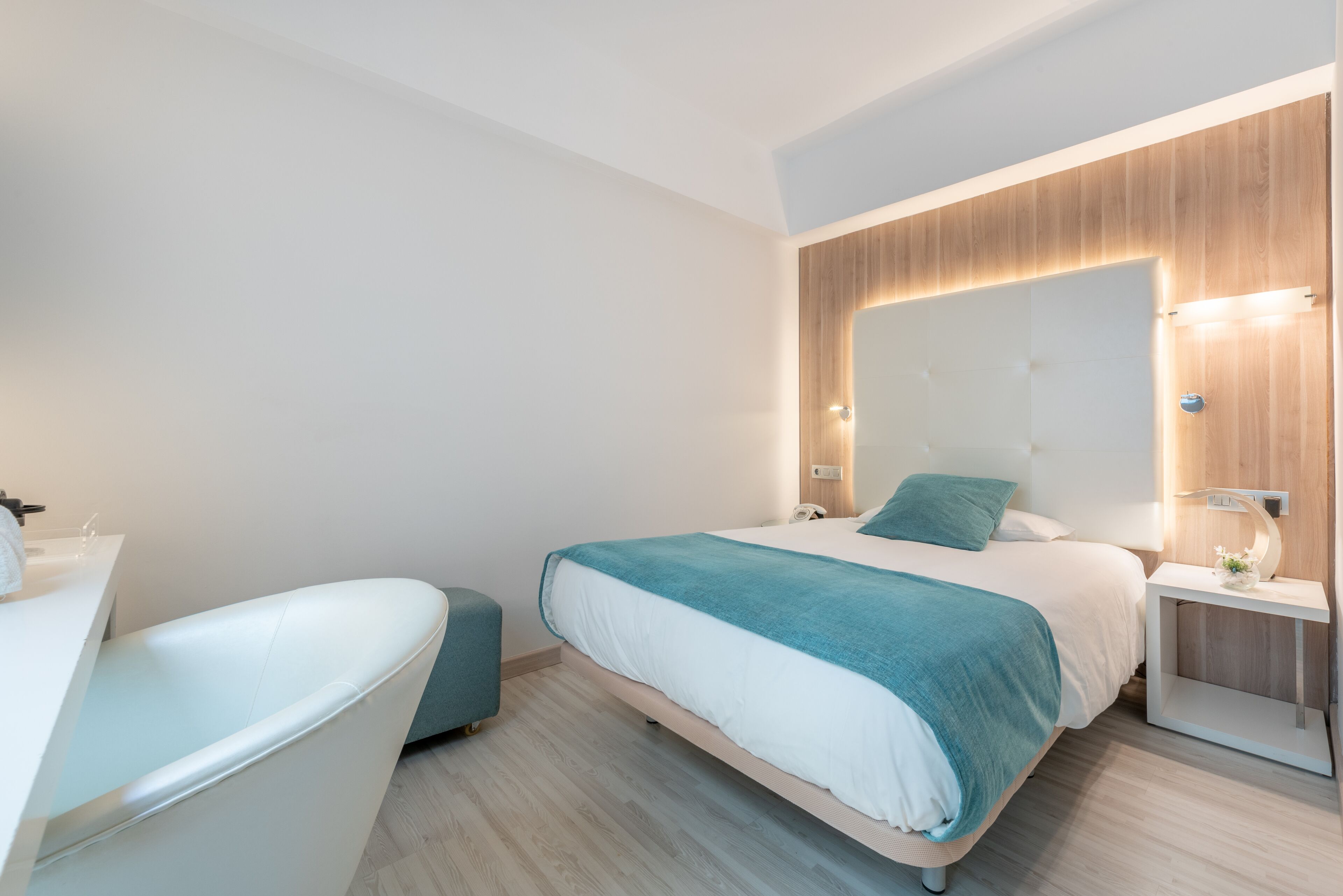 A modern hotel room with a bed, a white bathtub, a bedside table, and a large mirror.