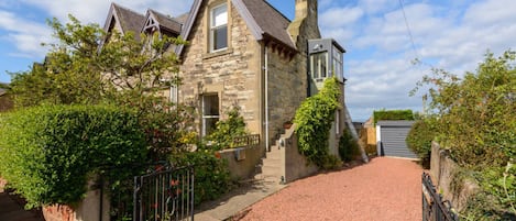 A stone house with a gravel driveway and a metal gate.