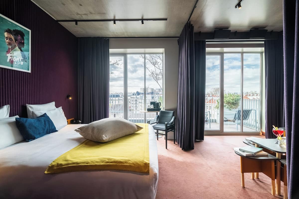 Une chambre d’hôtel équipée d’un lit, d’un bureau, d’une chaise et d’une grande fenêtre donnant sur la ville.