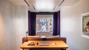 Een kamer met een houten bureau, een laptop, een afstandsbediening en een poster aan de muur.