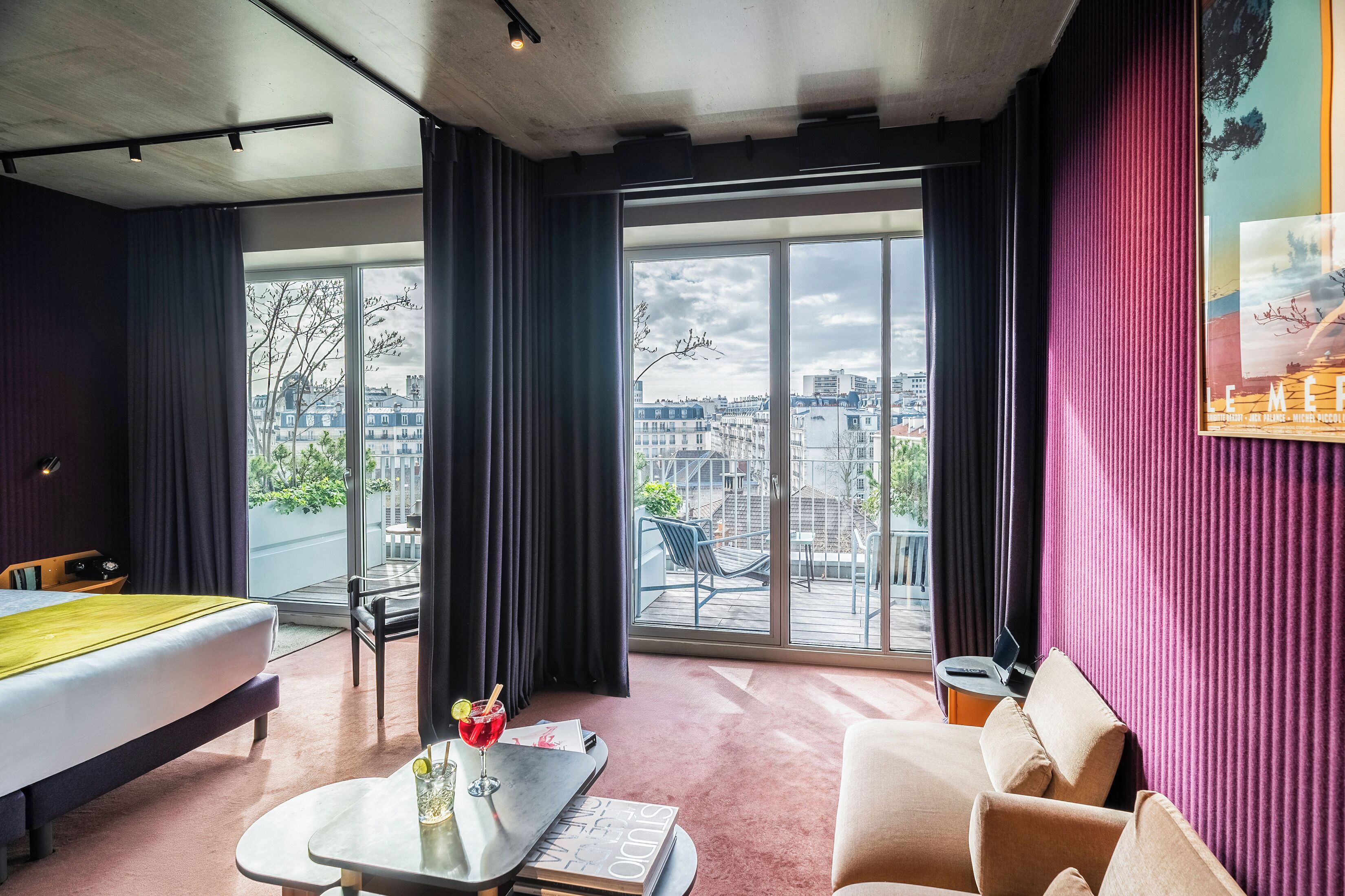 Une chambre d’hôtel avec un lit, une table avec une boisson, un canapé et un balcon offrant une vue sur la ville.