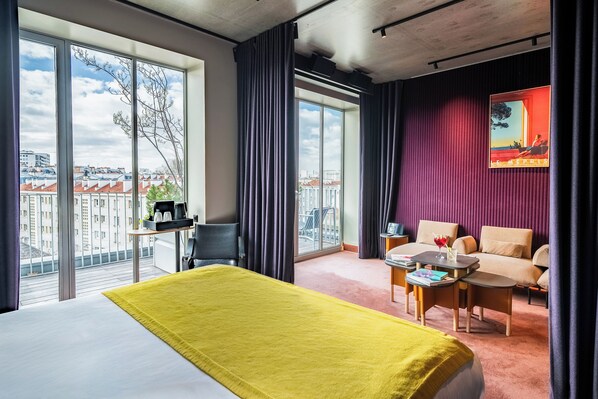 A hotel room with a bed, a sofa, a small table, and a balcony with a city view. - mk2 Hotel Paradiso Nation (Paris)