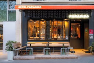 A hotel entrance with a sign reading 'HOTEL PARADISO,' a bench outside, and a staircase leading to the entrance.