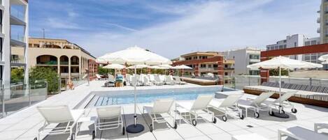 A rooftop pool area with lounge chairs and umbrellas, surrounded by buildings.