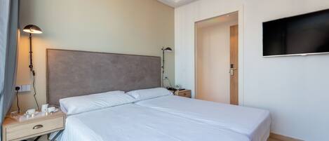 A hotel room with a large bed, bedside tables, a flat-screen TV, and a lamp.