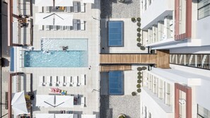 Vista aérea de un hotel moderno con piscina central, tumbonas y terraza de madera.
