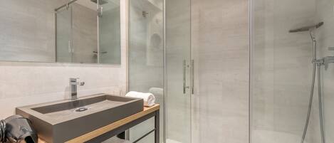 A modern bathroom with a glass shower enclosure, a large mirror, and a wooden vanity with a sink and towel storage.
