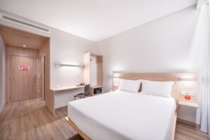 Een moderne hotelkamer met een groot bed, een bureau, een stoel, een garderobe en een spiegel.