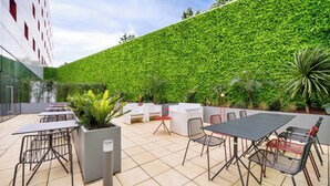 Une terrasse extérieure avec des tables et des chaises, un mur végétal et des plantes en pot.