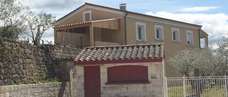 A two-story building with a stone wall and a small attached structure with a red door.