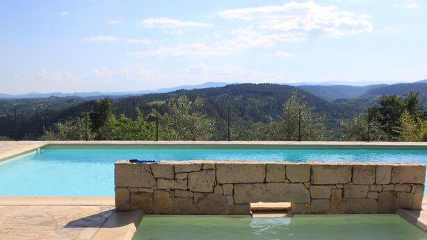 Una piscina con pared de piedra y agua cristalina, rodeada de un paisaje montañoso.