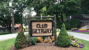A wooden sign with the words "CLUB GETAWAY" surrounded by landscaped bushes and flowers. - Club Getaway Valley View 1 (Kent)