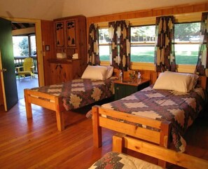 Two beds feature geometric-patterned quilts, complemented by a wooden cabinet, mirror, and a small table with a vase of flowers.