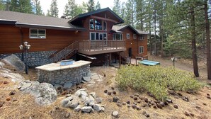 A two-story wooden cabin with a stone foundation, a deck, and a stone wall. - 5 Bedroom close to Town, hot tub, BBQ(SL437) (Stateline)