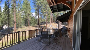 A wooden deck with outdoor furniture, surrounded by tall pine trees. - 5 Bedroom close to Town, hot tub, BBQ(SL437) (Stateline)