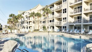 Une piscine dont la profondeur maximale est indiquée à 6 pieds, entourée de chaises longues et bordée d’un immeuble à plusieurs étages doté de balcons.