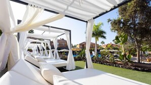 Un área de descanso al aire libre techada con canopies blancos y sillones reclinables con cojines blancos.