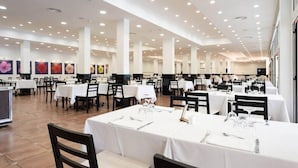 Un comedor amplio con varias mesas y sillas, manteles blancos e iluminación en el techo.