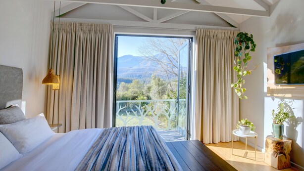 Une chambre avec un grand lit, une vue sur les montagnes et un balcon avec des rideaux.
