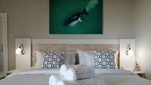 Une chambre d’hôtel avec un lit, des coussins à motifs, une œuvre d’art représentant une baleine accrochée au mur et des lampes de chevet.