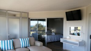 Une chambre d’hôtel moderne équipée d’un canapé, d’une petite table, d’une table de chevet avec une lampe, d’un téléviseur fixé au mur et d’un balcon avec vue.