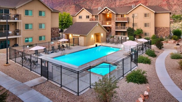 A hotel with a swimming pool, outdoor seating, and a view of red rock formations. - 6B Cozy Moab Redcliff Condo, Pet Friendly, Pool & Hot Tub (Moab)