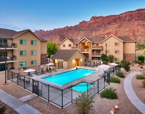A hotel with a swimming pool, outdoor seating, and a view of red rock formations. - 6B Cozy Moab Redcliff Condo, Pet Friendly, Pool & Hot Tub (Moab)