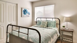 A bedroom with a bed, a bedside table with a lamp, a window with blinds, and a door. - 6B Cozy Moab Redcliff Condo, Pet Friendly, Pool & Hot Tub (Moab)