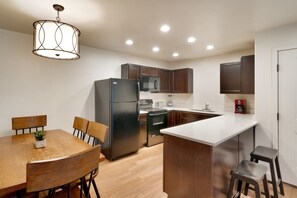 A modern kitchen with a central island, wooden cabinets, and a dining area with a table and chairs. - 6B Cozy Moab Redcliff Condo, Pet Friendly, Pool & Hot Tub (Moab)
